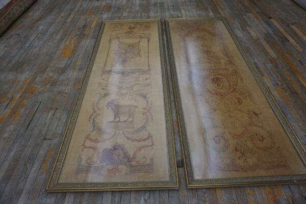 Two framed, elongated beige textiles with classical red and blue patterns rest on worn gray wood flooring.