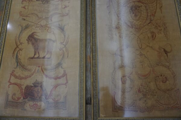 Two framed tapestry panels show faded pastoral scenes, including a goat and floral scrolls, against a tan background.