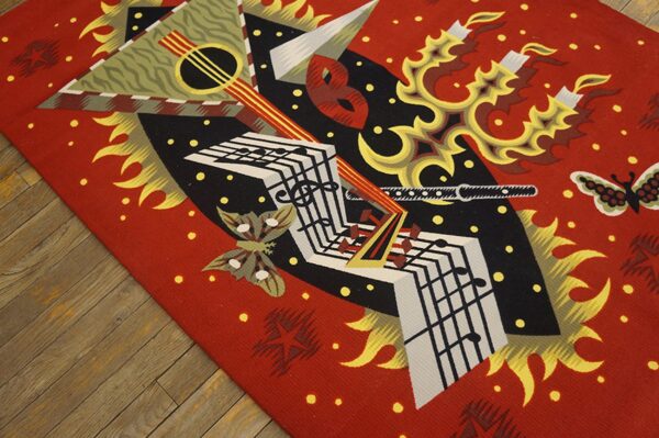 Red, black, and gold flatweave rug with abstract musical and flame motifs rests on rustic wooden flooring.