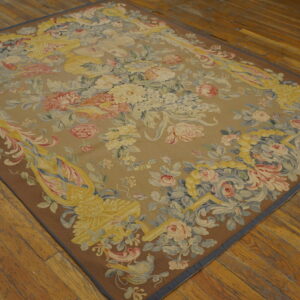 Rectangular tapestry rug with pastel floral bouquets and scrollwork on a tan field over wood planks.