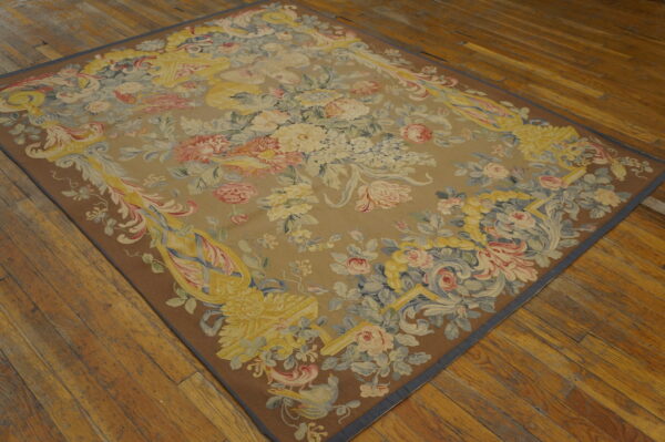 Rectangular tapestry rug with pastel floral bouquets and scrollwork on a tan field over wood planks.