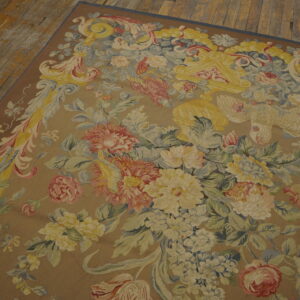 Muted floral tapestry-style rug in tan, yellow, pink, and blue resting on wooden floorboards.