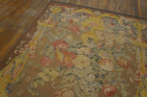 Muted floral tapestry-style rug in tan, yellow, pink, and blue resting on wooden floorboards.
