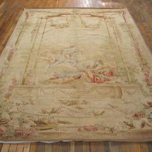 Large light beige rug featuring a central figurative scene, floral borders, birds, and animals on wood plank flooring.