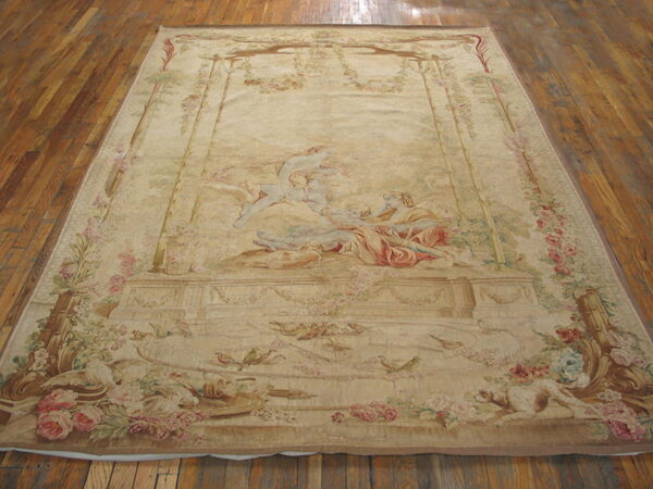 Large light beige rug featuring a central figurative scene, floral borders, birds, and animals on wood plank flooring.