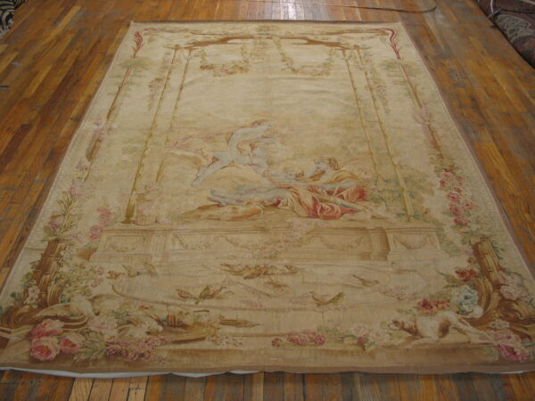 Faded beige, pink, and green tapestry rug displaying a large neoclassical scene on wood planks.