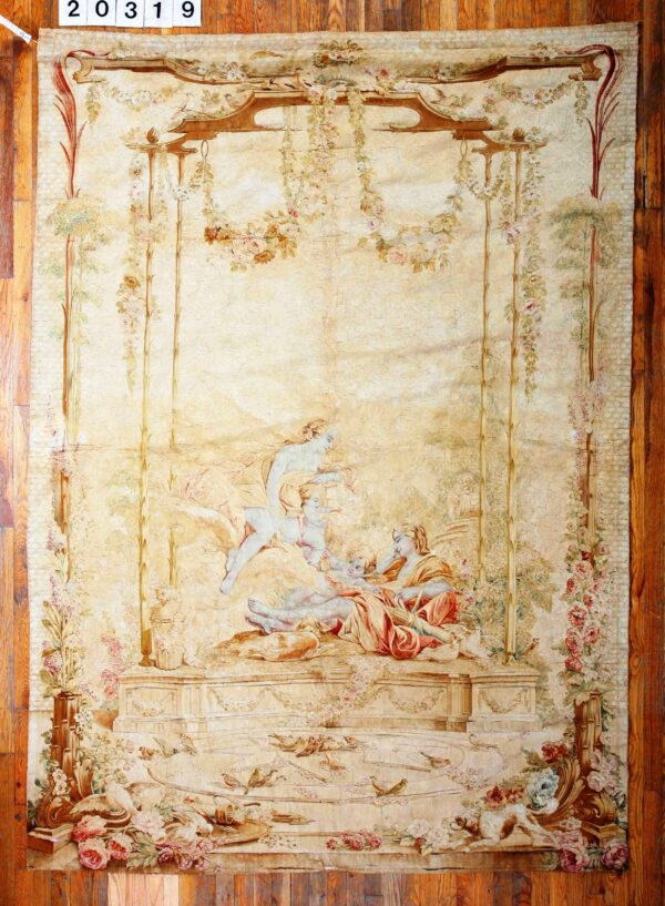Cream-colored pictorial textile depicting three figures in a garden setting surrounded by vines and birds on wood flooring.