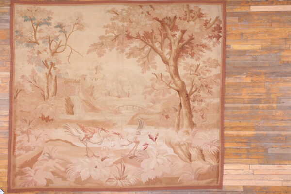 Beige and brown low-pile rug displaying a scenic pastoral pattern with trees and two stylized birds on wood flooring.