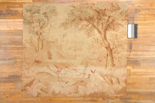 Tan and beige low-pile scenic rug featuring a pastoral landscape with trees and large wading birds on wood flooring.