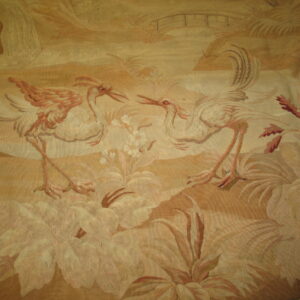 Tonal tan and cream low-pile rug displays two long-legged birds amid a detailed floral landscape and bridge.