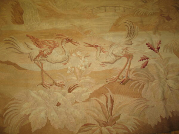 Tonal tan and cream low-pile rug displays two long-legged birds amid a detailed floral landscape and bridge.