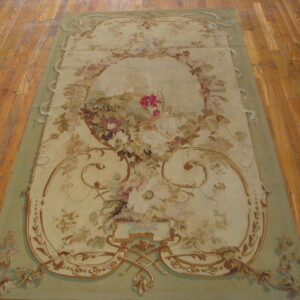 Ornate pale green and cream rug displaying a large central floral bouquet and brown scrollwork on plank flooring.