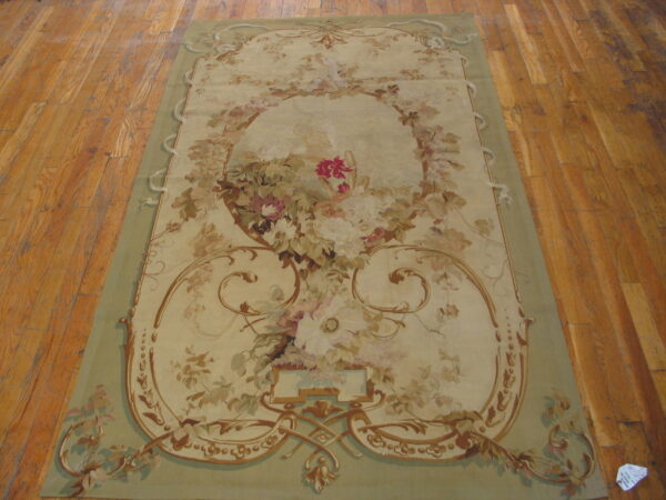 Ornate pale green and cream rug displaying a large central floral bouquet and brown scrollwork on plank flooring.