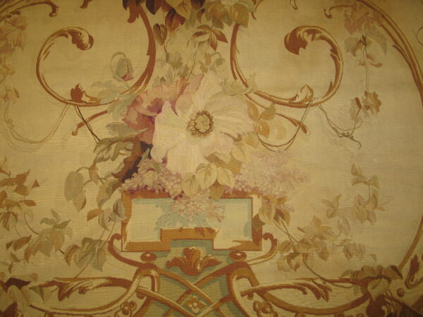 Tapestry-style rug detail featuring a large floral bouquet and brown ornamental scrollwork on a beige ground.