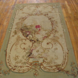 Low-pile beige rug with a sage border and elaborate pastel floral pattern rests on wood planks.