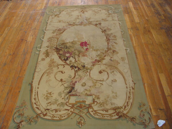 Low-pile beige rug with a sage border and elaborate pastel floral pattern rests on wood planks.