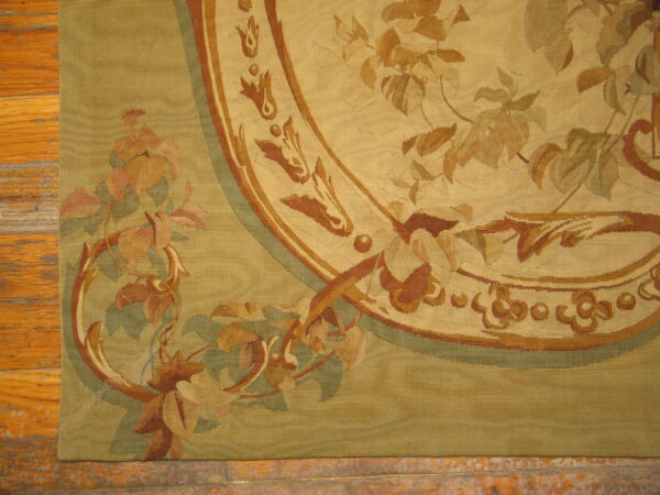 Detail of a low-profile rug with a gold and green background and elaborate floral medallions on wood planks.