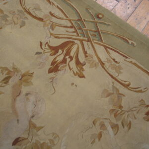 Low-pile beige rug with rust, green, and rose floral patterns resting on distressed hardwood flooring.