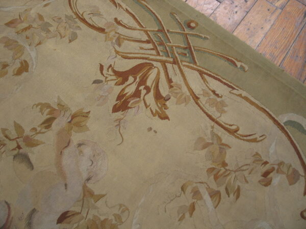 Low-pile beige rug with rust, green, and rose floral patterns resting on distressed hardwood flooring.