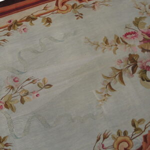Low-pile rug with a pale blue field framed by pink and brown floral borders and striped edges.