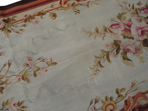 Low-pile rug with a pale blue field framed by pink and brown floral borders and striped edges.