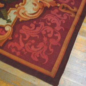 Low-pile rug with ornate burgundy, red, and orange scrollwork rests on light, distressed wood floors.
