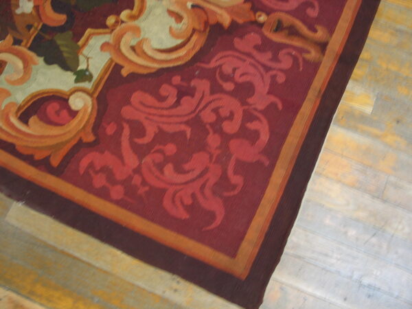 Low-pile rug with ornate burgundy, red, and orange scrollwork rests on light, distressed wood floors.