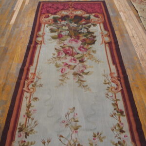 Pale blue runner rug with intricate floral pattern and a wide burgundy and orange ornamental border on wood flooring.