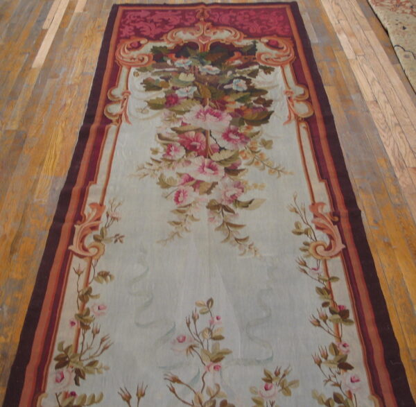 Pale blue runner rug with intricate floral pattern and a wide burgundy and orange ornamental border on wood flooring.