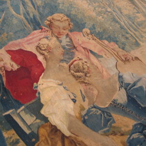 Close-up of a low-pile tapestry rug patterned with two figures in blue, dusty rose, red, and tan colors.