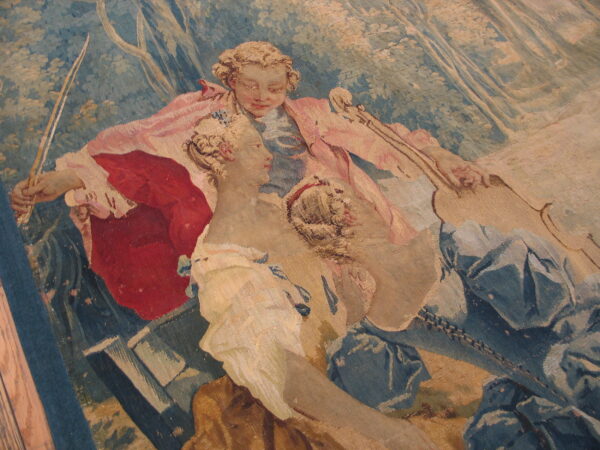 Close-up of a low-pile tapestry rug patterned with two figures in blue, dusty rose, red, and tan colors.
