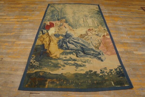 Low-pile tapestry rug depicting a pastoral scene in muted blues, greens, and pinks on a wood floor.