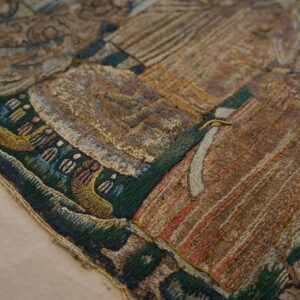Varied texture embroidery close-up in gold, brown, and green, showing geometric and figurative details on beige.