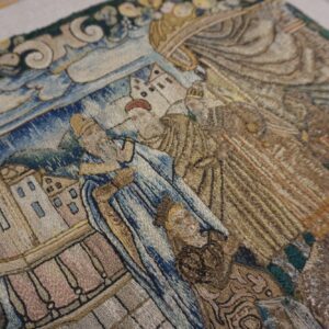 Muted blue and brown embroidered rug detail depicting a narrative scene with figures and architecture.