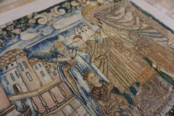 Muted blue and brown embroidered rug detail depicting a narrative scene with figures and architecture.