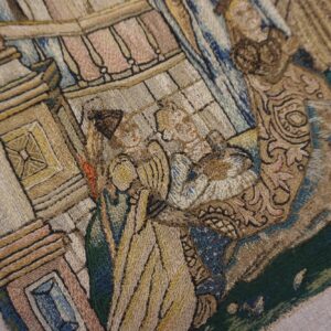 Detail of an embroidered textile featuring a figurative scene with tan, brown, blue, and green threads.