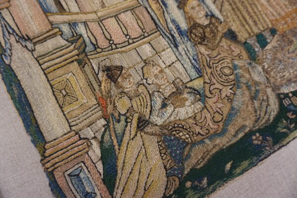 Detail of an embroidered textile featuring a figurative scene with tan, brown, blue, and green threads.