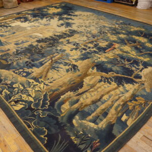 Low-pile tapestry rug with a blue and gold pictorial forest scene and wildlife rests on hardwood flooring.