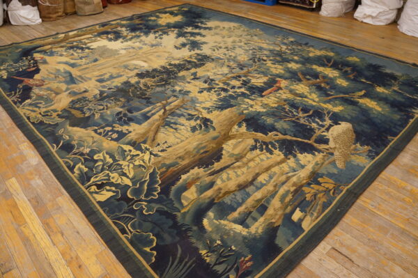 Low-pile tapestry rug with a blue and gold pictorial forest scene and wildlife rests on hardwood flooring.