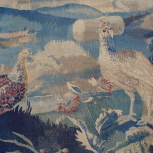 Woven textile detail showing two large birds with blue and red feathers set against a blue and beige landscape.