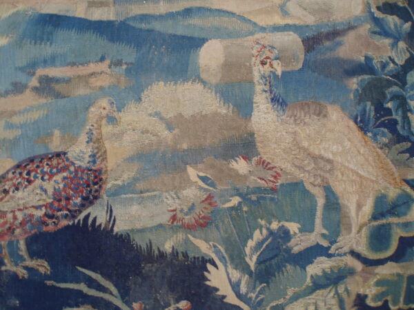Woven textile detail showing two large birds with blue and red feathers set against a blue and beige landscape.