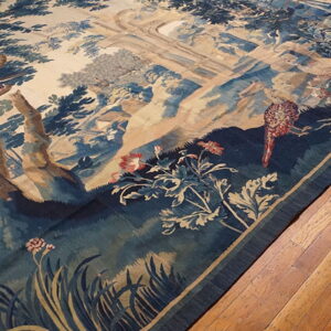 Low-pile rug with detailed blue and tan forest tapestry design resting on wooden flooring.