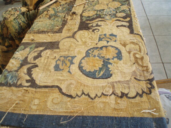 Ornate yellow, blue, and brown low-pile rug fragment with detailed floral motifs resting on a gray tile floor.