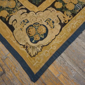 A low-pile rug corner featuring yellow flowers and blue borders rests on rustic wooden plank flooring.