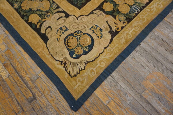 A low-pile rug corner featuring yellow flowers and blue borders rests on rustic wooden plank flooring.
