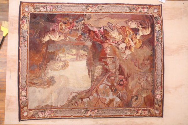 Muted, flatwoven rug with a detailed figural tapestry pattern in warm colors, framed by a floral border.
