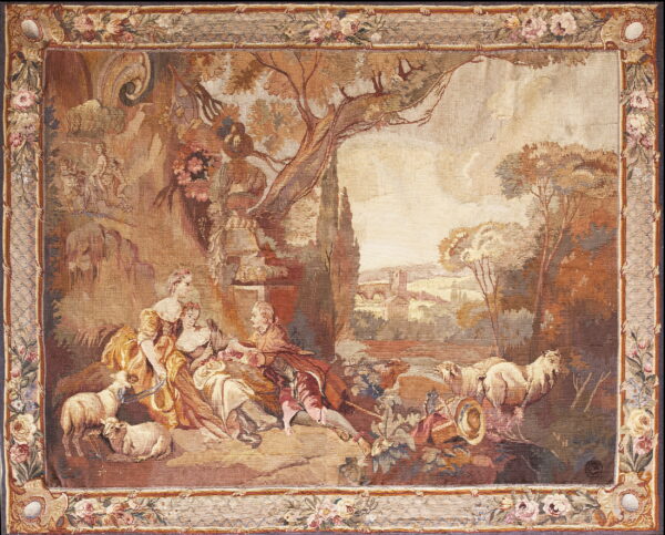 Tapestry rug featuring a pastoral scene with figures and sheep framed by a floral border in muted earth tones.