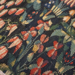 Close-up of a dark blue flatweave rug with a rustic floral pattern in red, teal, and gold tones.