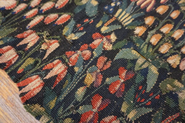 Close-up of a dark blue flatweave rug with a rustic floral pattern in red, teal, and gold tones.