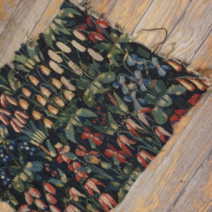 A frayed flatweave rug remnant with a dark floral pattern rests on distressed wooden floorboards.